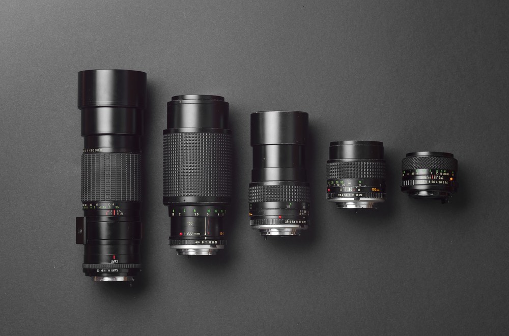 A collection of camera lenses, showing the differences in dimension of a telephoto compared to a wide-angle prime lens, with much in between.