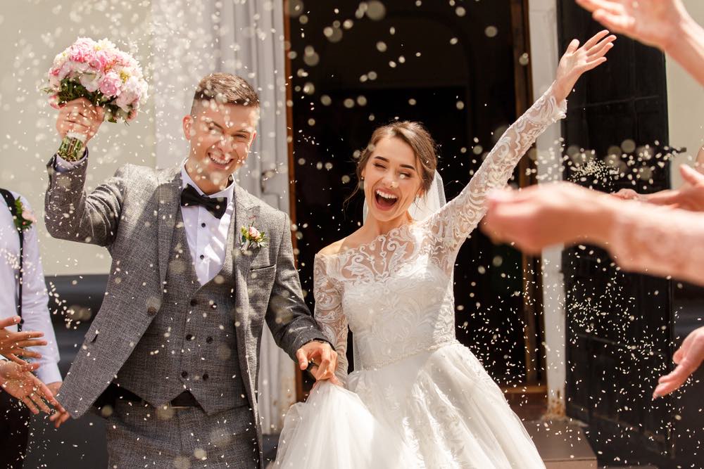 A traditional wedding photo of a bride and groom after the ceremony being showered with confetti as they leave the ceremony venue.