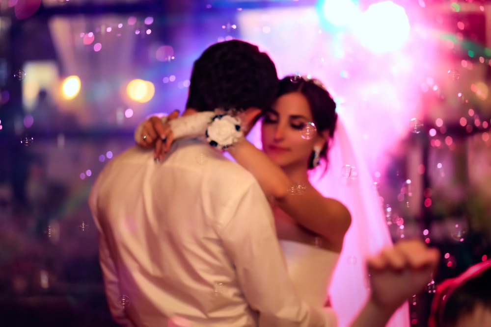 A bride and groom are dancing while there is a bokeh effect in the background.