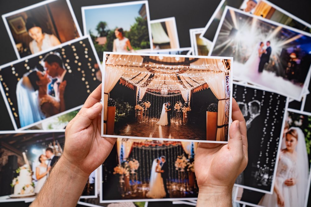 A pair of hands holing a wedding photo with a collage of other wedding photos that are slightly blurry in the background.