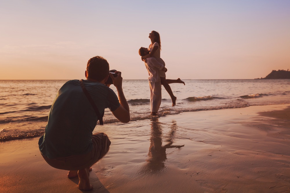 A photographer is photographing a wedding couple during sunset for a silhouette effect. 