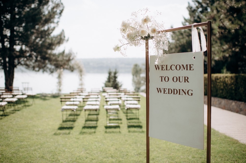 A photo of an outdoor ceremony with rows of empty chairs and a sign that says "welcome to our wedding".